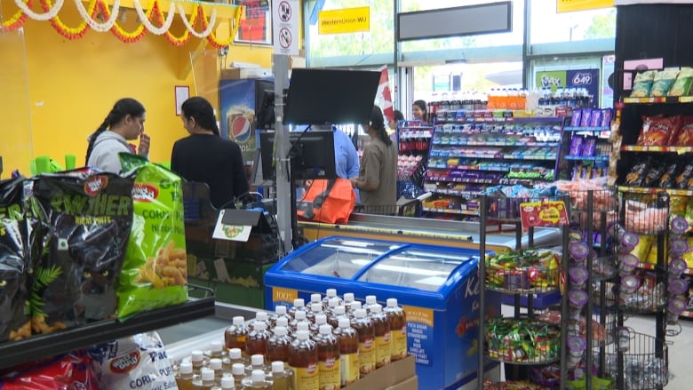 Inside a grocery store with a couple of people and shelves full of items.