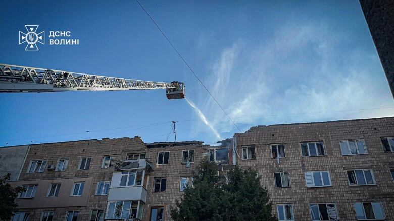 A low-rise building is shown. It appears to be a residential building and part of its roof is missing as a crane overhead is shown, with water appearing to be sprayed from the crane.