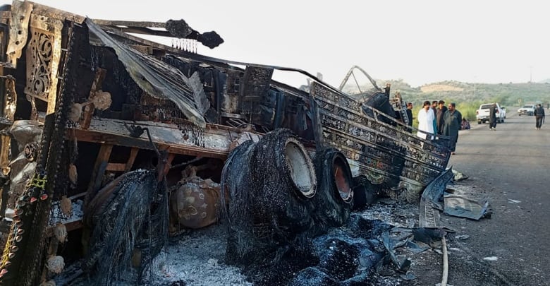 People look at a burnt vehicle on a road in Pakistan. 