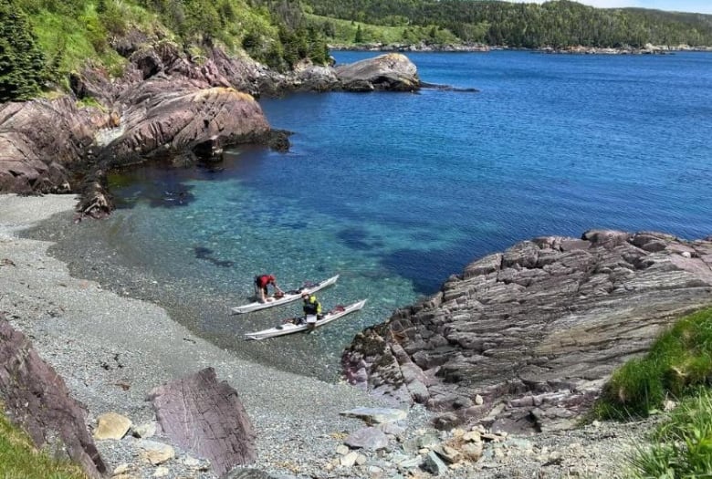 Kayakers in their boats in a cove, in bright-blue waters.