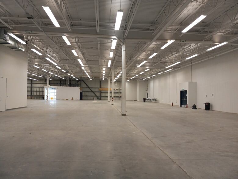 A massive empty building that has bright lights over head and white walls and concrete floor.