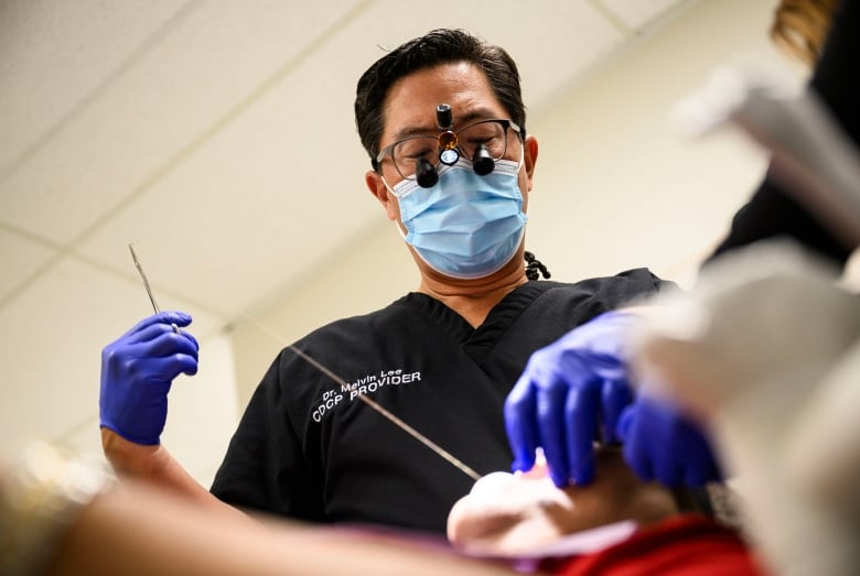 A dentist stitches someone up after taking out one of their teeth.