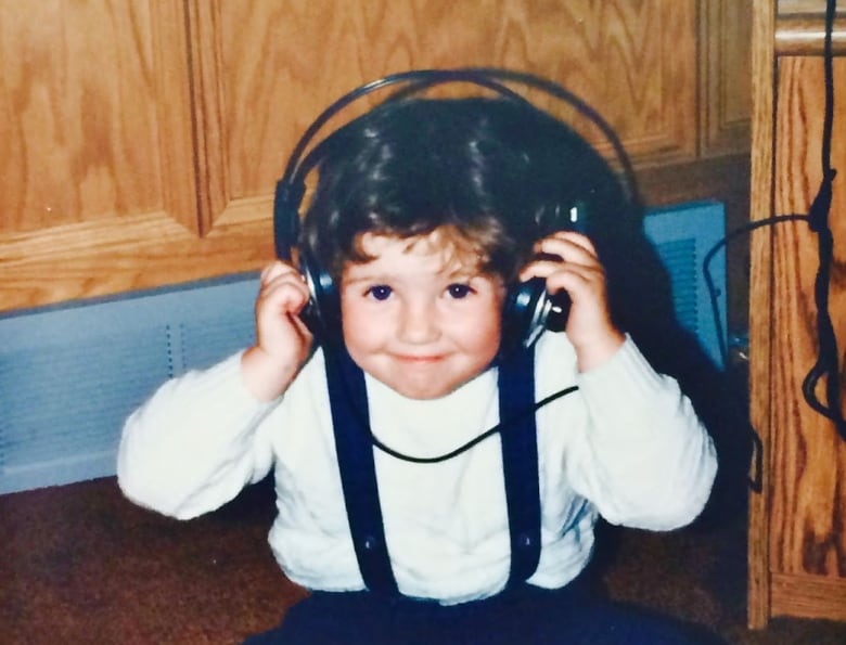 A toddler grins at the camera as she puts on a pair of headphones. 