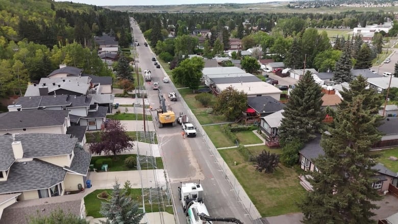 a street with houses on both sides is fenced off for construction in the middle of the road.