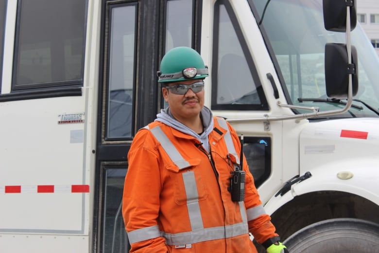 A man in an orange suit in front of a white bus.