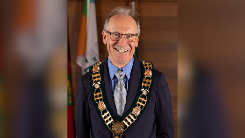 A person wearing a suit and a gold chain of office is seen smiling.