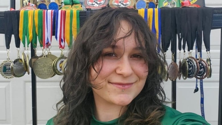 A young woman sits in front of a rack of medals and trophies