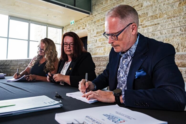 Three people are seated at a table to sign a contract.