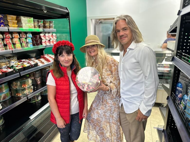 A woman poses with a cake along between a man and a woman in red. 