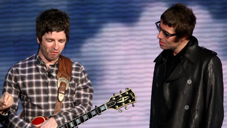 Two British rockstars onstage. One has a guitar.