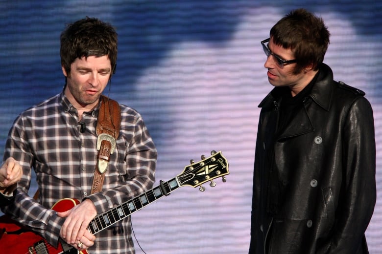 Two British rockstars onstage. One has a guitar.