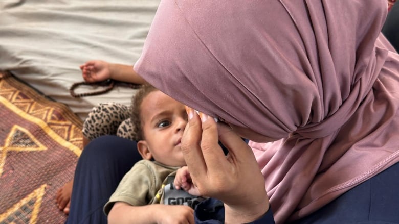 a baby lays in his mom's laps as she wipes a tear from her eyes