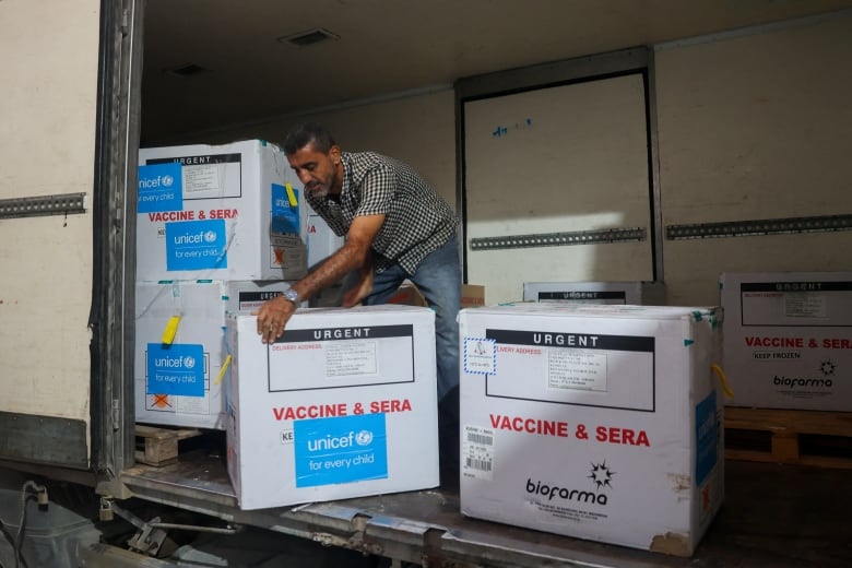 A man unloads boxes from the back of a truck. The boxes are marked 'URGENT' and 'VACCINE & SERA.' They are branded 