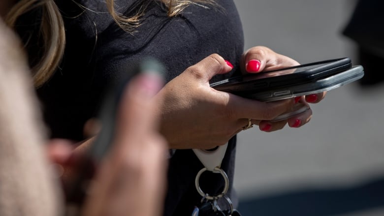 A hand holds a cellphone with both thumbs pressed on the screen as car keys dangle from their fingers.