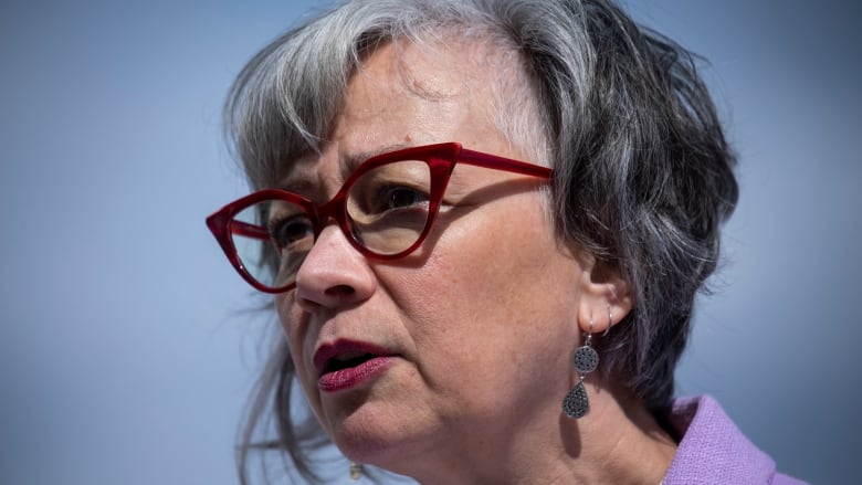 A close up shot of a woman wearing red glasses and a purple shirt. 