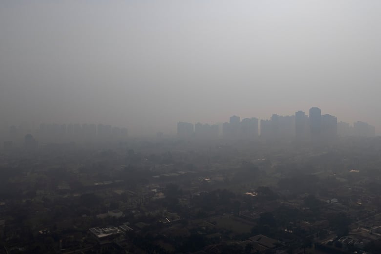 An aerial view of a cityscape drenched in a thick gray smoke, its buildings barely visible against the darkened sky. 