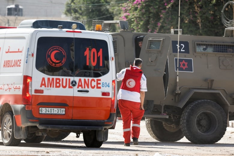 A paramedic walks in between an ambulance and a military vehicle. 