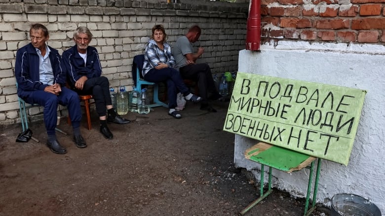 Russian local residents sit near a shelter where they were hiding during a recent fighting between Ukrainian and Russian forces in the town of Sudzha that is controlled by Ukrainian army, Kursk region, Russia August 16, 2024. The sign on the poster reads: 