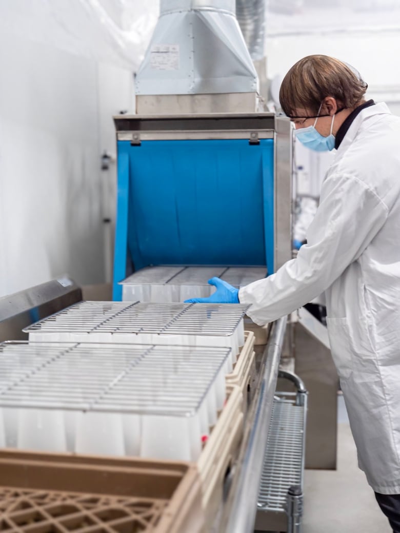 A person in a lab coat puts cups through an industrial dishwasher