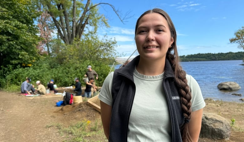 An archaeological supervisor poses for a photo near a dig site along a river.