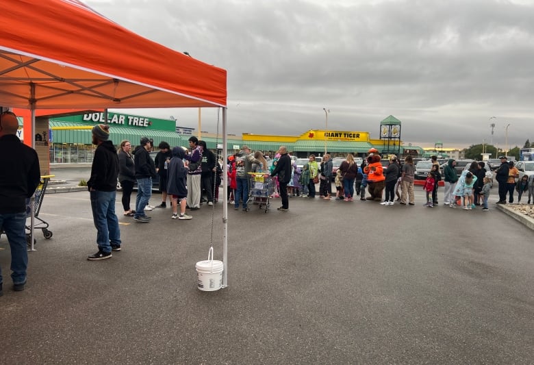 people are lined up in a parking lot with a giant tiger and dollar store in the background