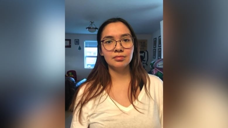 A young woman with glasses standing in a living room.