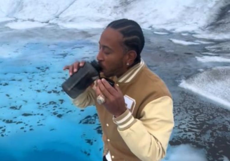 A man drinks from a water bottle near a pool of icy water.