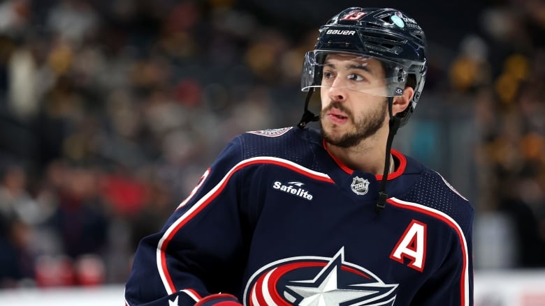 A men's hockey player wearing a dark blue jersey and helmet looks to the left.