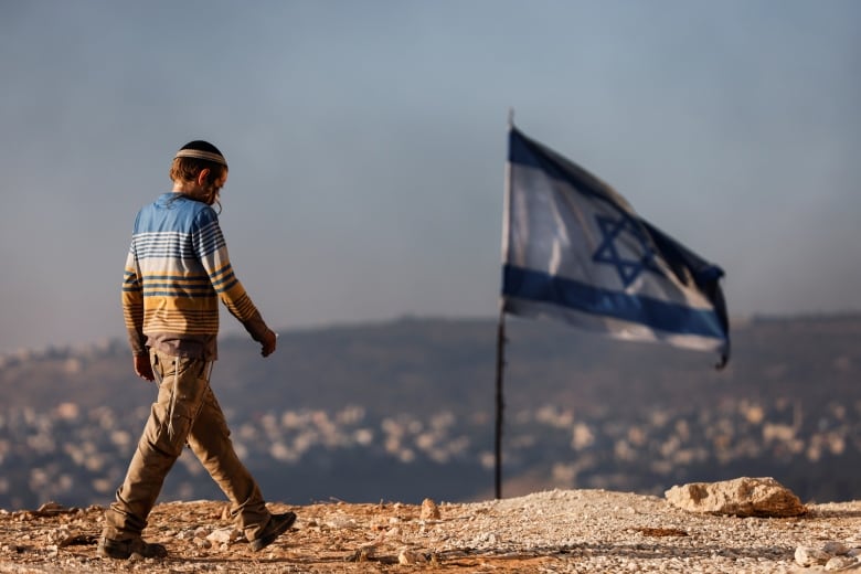 A Jewish settler teenager walks by an Israeli flag in Givat Eviatar, a new Israeli settler outpost, near the Palestinian village of Beita in the Israeli-occupied West Bank June 23, 2021. Picture taken June 23, 2021.