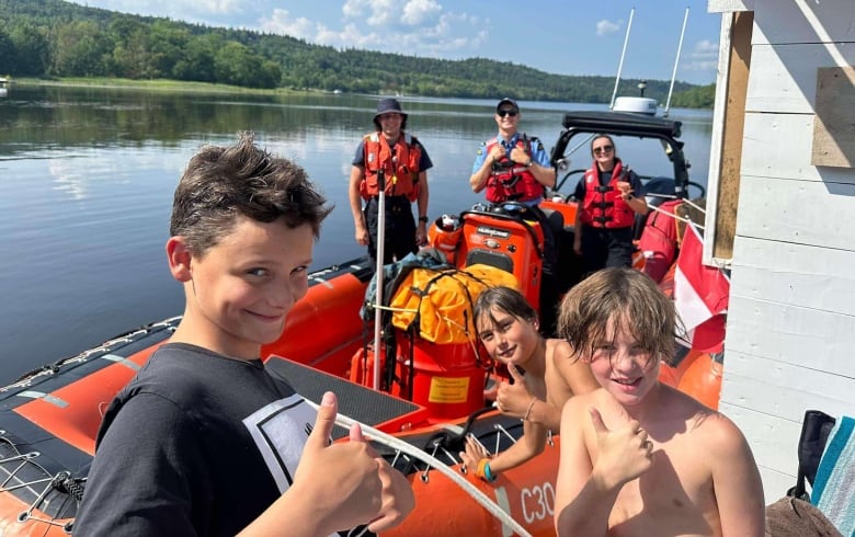 Three people on a coast guard boat pose with three young boys. 