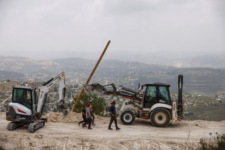 Israeli settlers walk past construction machinery after structures were erected for a new Jewish seminary school, in the settler outpost of Homesh in the Israeli-occupied West Bank May 29, 2023 