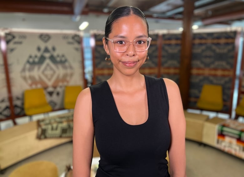 Woman stands for photo wearing clear glasses and black tank top. 