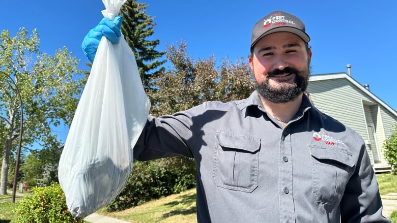 a man in a grey shirt holds up a white garbage bag with something in it.