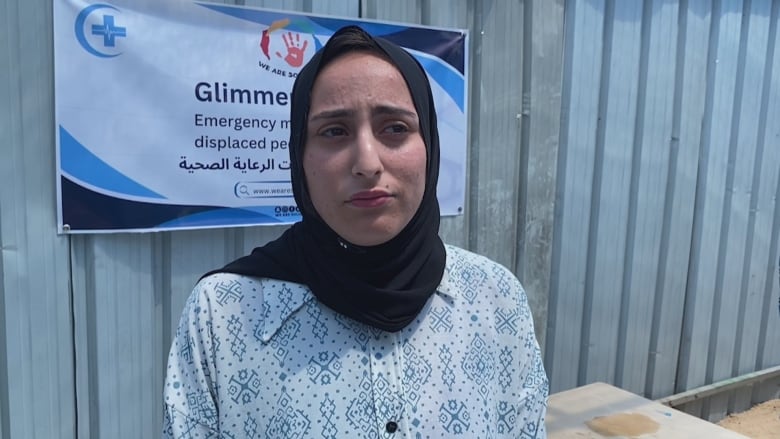 A woman in a white shirt and blue headscarf stands outside