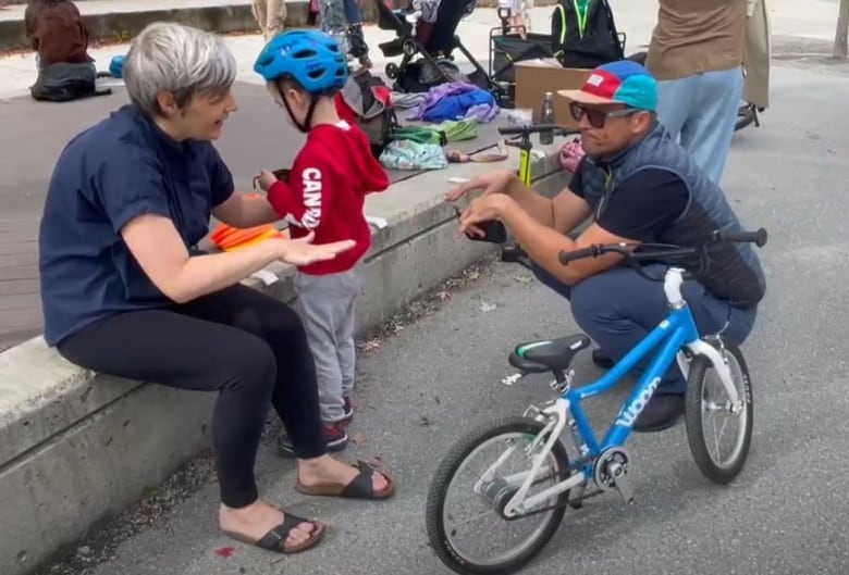 man talks to woman with child and small bike in frame