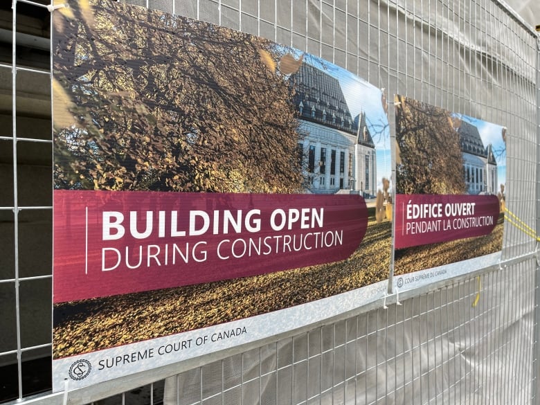 A sign is posted on a metal construction fence. It reads 