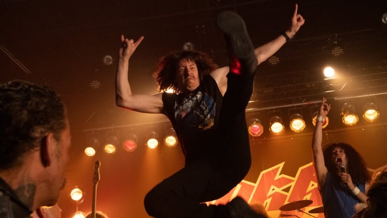 A man leaps in the air at a rock concert in a still from a movie.