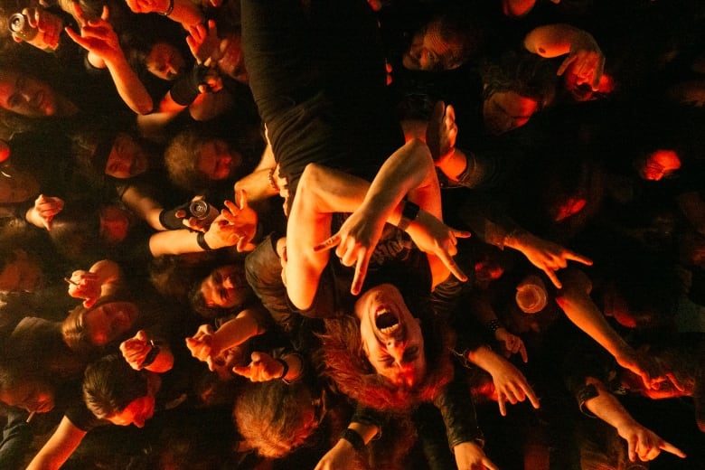 A still from a film shows a man crossing his arms and shouting as he crowd surfs.