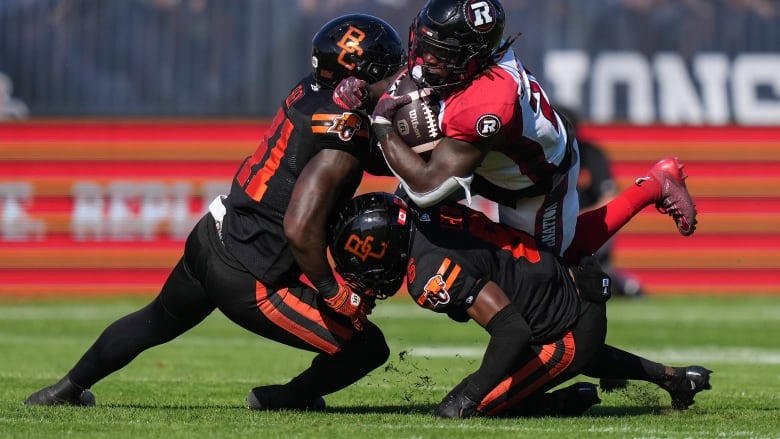 Three football players collide in the field.