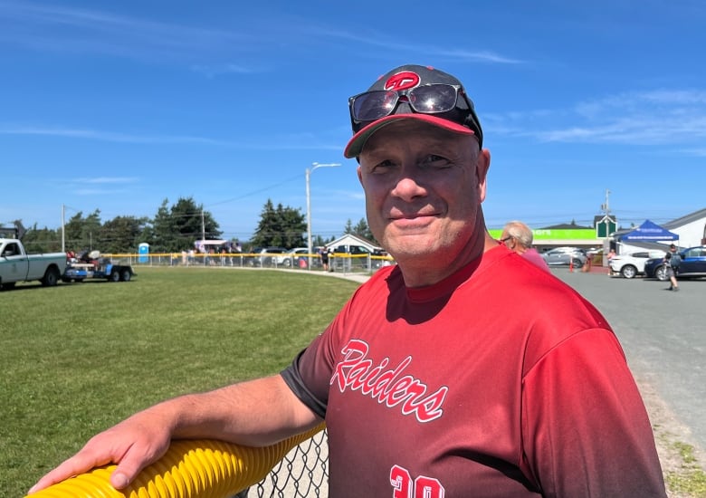 A man smiles. He wears a jersey that reads 