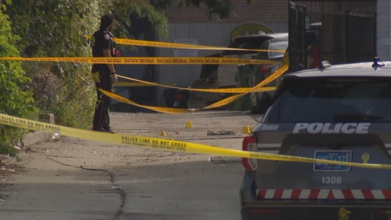 A police officer stands in a back alleyway surrounded by yellow tape.