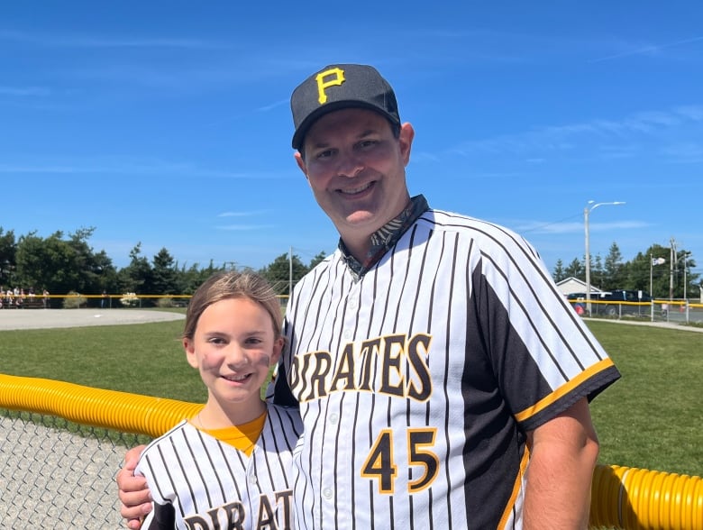 A man on the right has his arm around a girl on the left. Both wear jerseys that read 