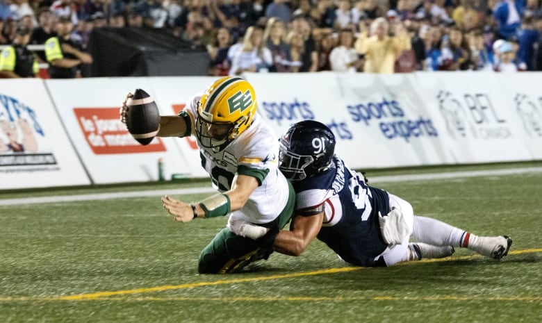 A man in a blue football uniform tackles a man wearing a white and green football uniform on a field.