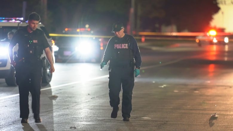 Police officers seen walking on a blocked off stretch of a street.