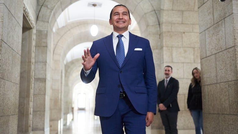 A man in a dark blue suit waves his hand.