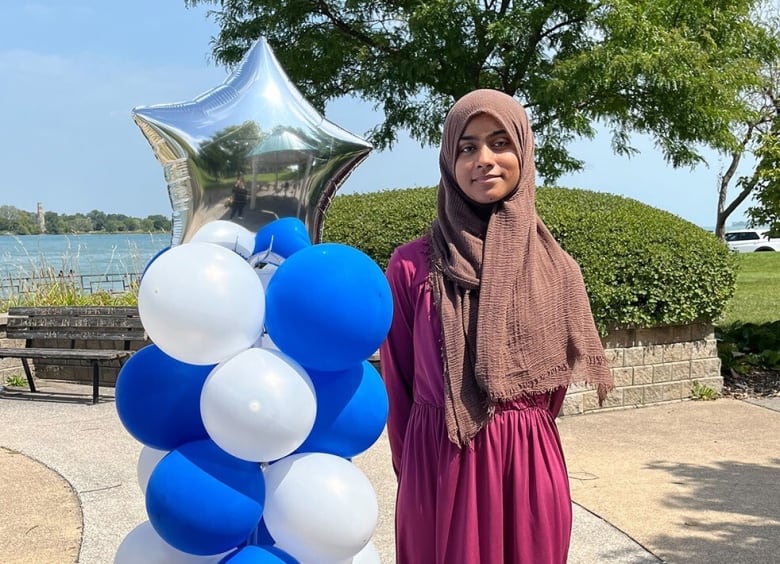 A Muslim woman stands next to decorative balloons.