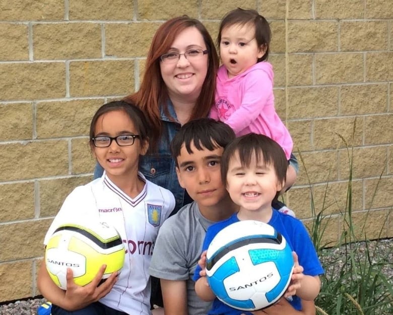 A woman sits with five children surrounding her. 