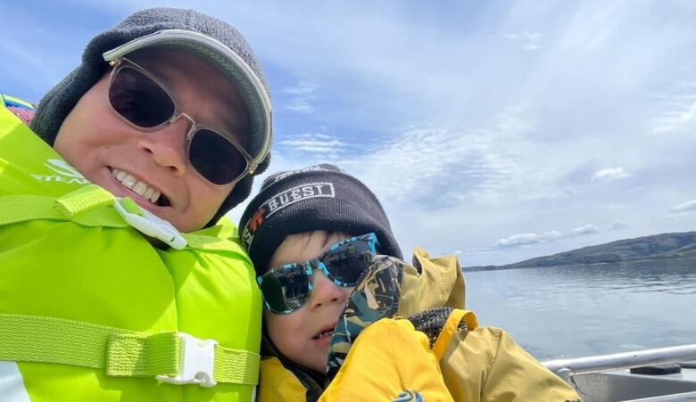 A woman and young child sit on a boat wearing liftjackets. 