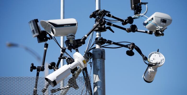 A bunch of security cameras mounted at the top of a pole and pointing in different directions, are depicted. 