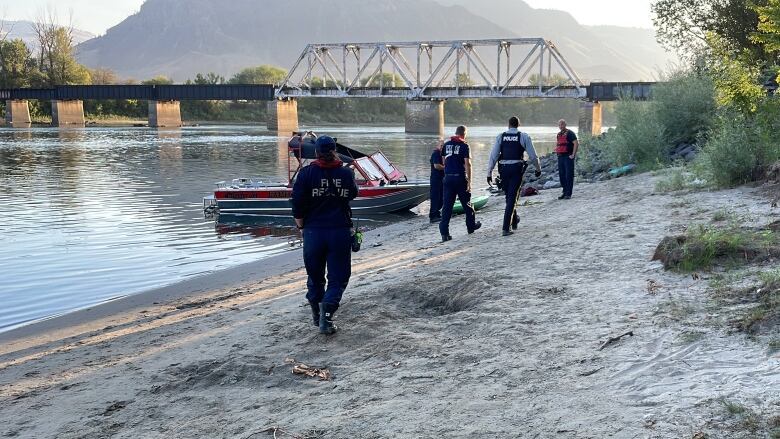 People wearing fire rescue and police uniforms walk along the shores of a river toward a rescue boat/